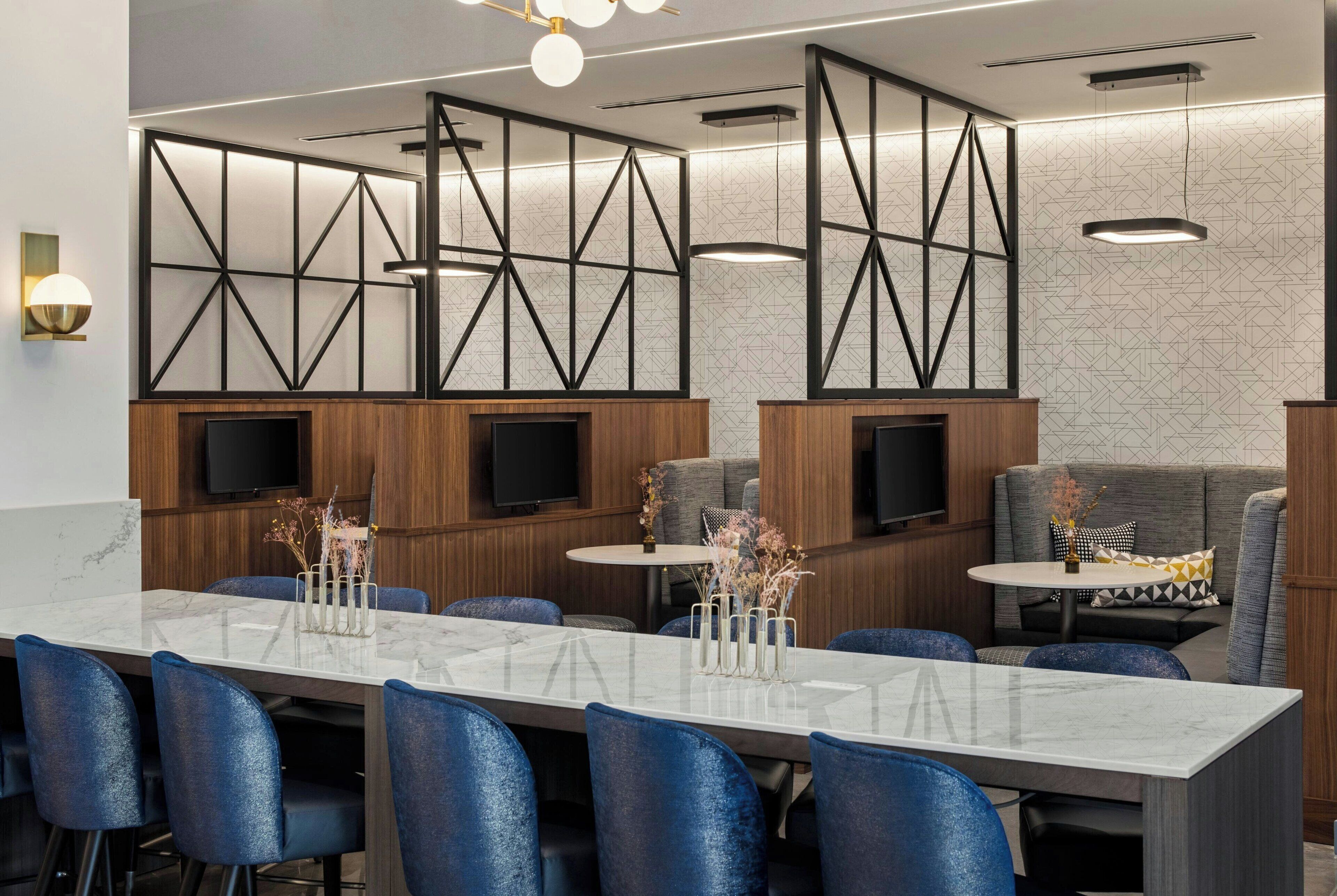 A modern hotel lobby with a marble reception desk, blue chairs, a sofa, and a TV screen.