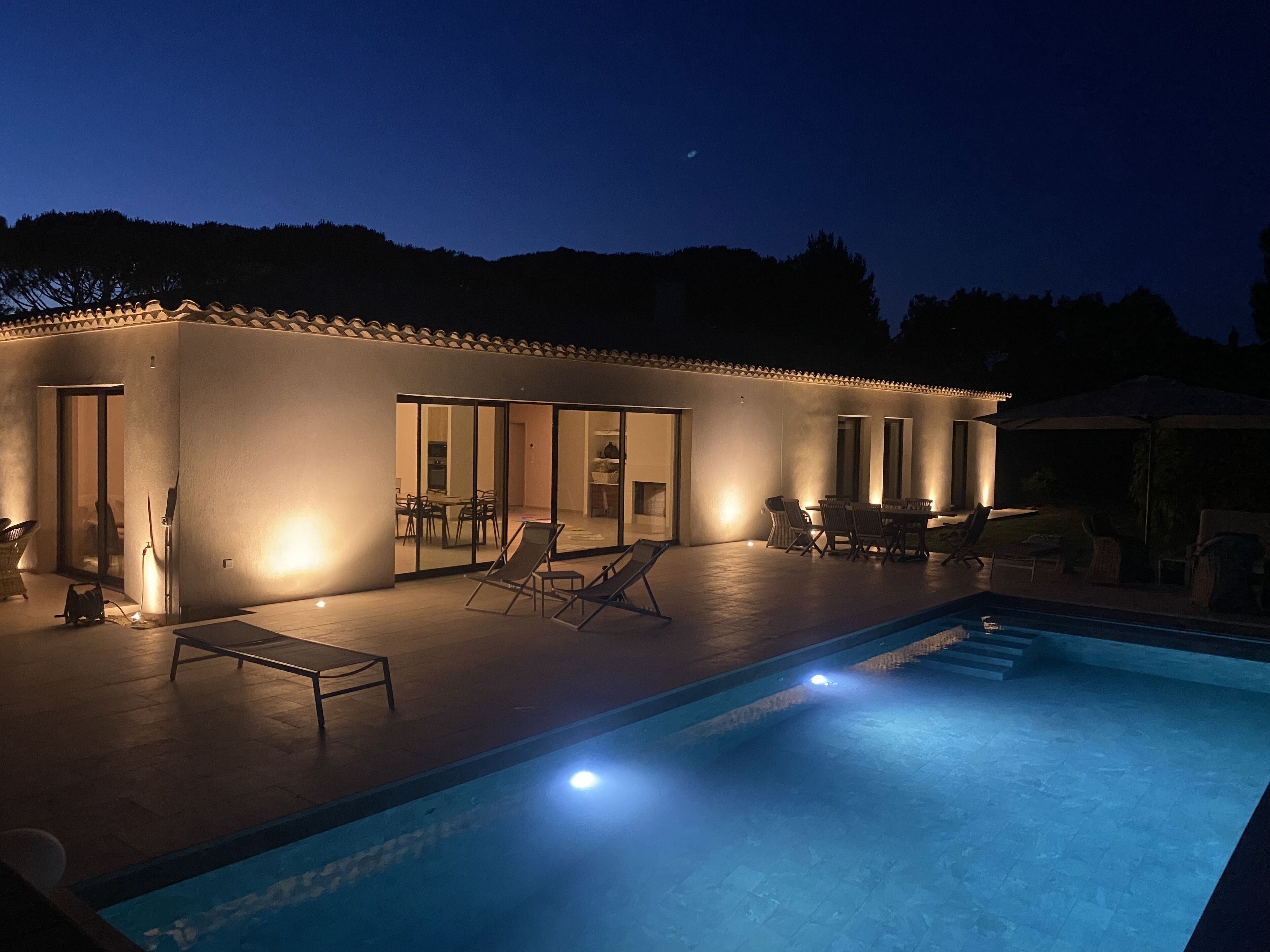 Una casa moderna con piscina, area salotto esterna e patio ben illuminato.