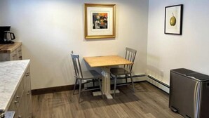 Une cuisine de taille réduite, avec une table et des chaises en bois, un réfrigérateur et des œuvres d’art encadrées accrochées aux murs.