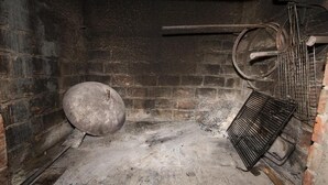 Une pièce aux murs de pierre, avec un grand objet rond en métal posé sur le sol et un support métallique doté d’une poignée incurvée, adossé au mur.
