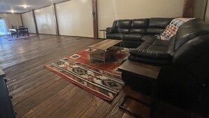 A spacious living room with a wooden floor, a black leather sofa, and a coffee table.