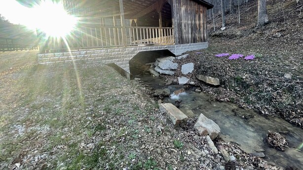 A wooden covered bridge with a stone pathway leading to a small stream.