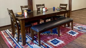 A dining area with a wooden table, four chairs, a bench, and a colorful rug.