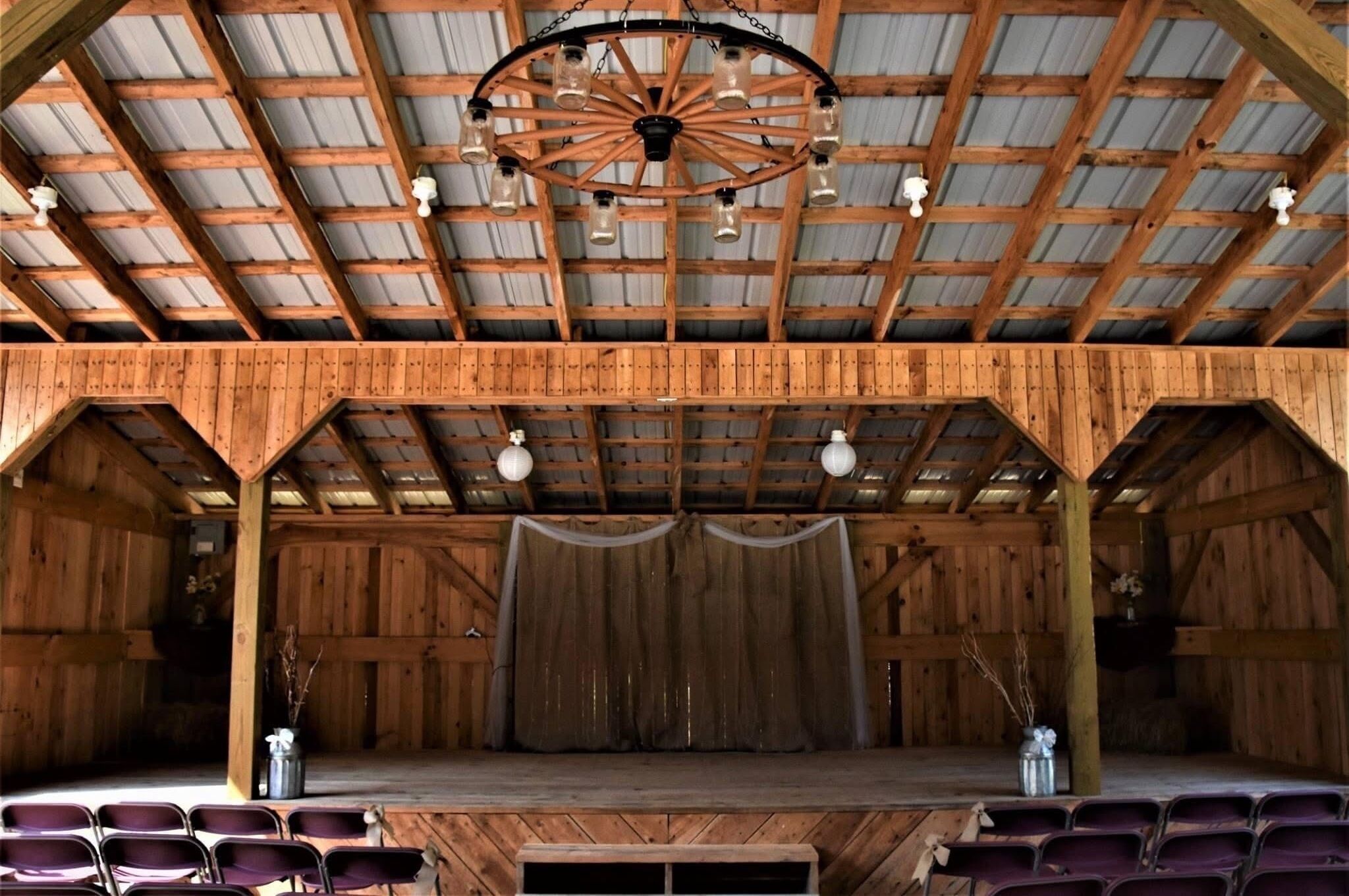 A rustic barn-style venue with a stage, wooden beams, and a ceiling fan.