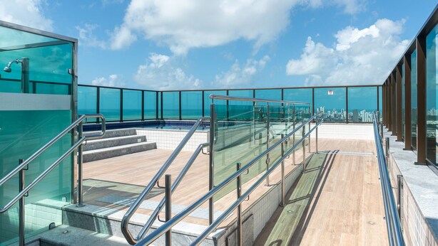Una terraza moderna al aire libre con barandas de vidrio, una piscina y vistas a la ciudad.