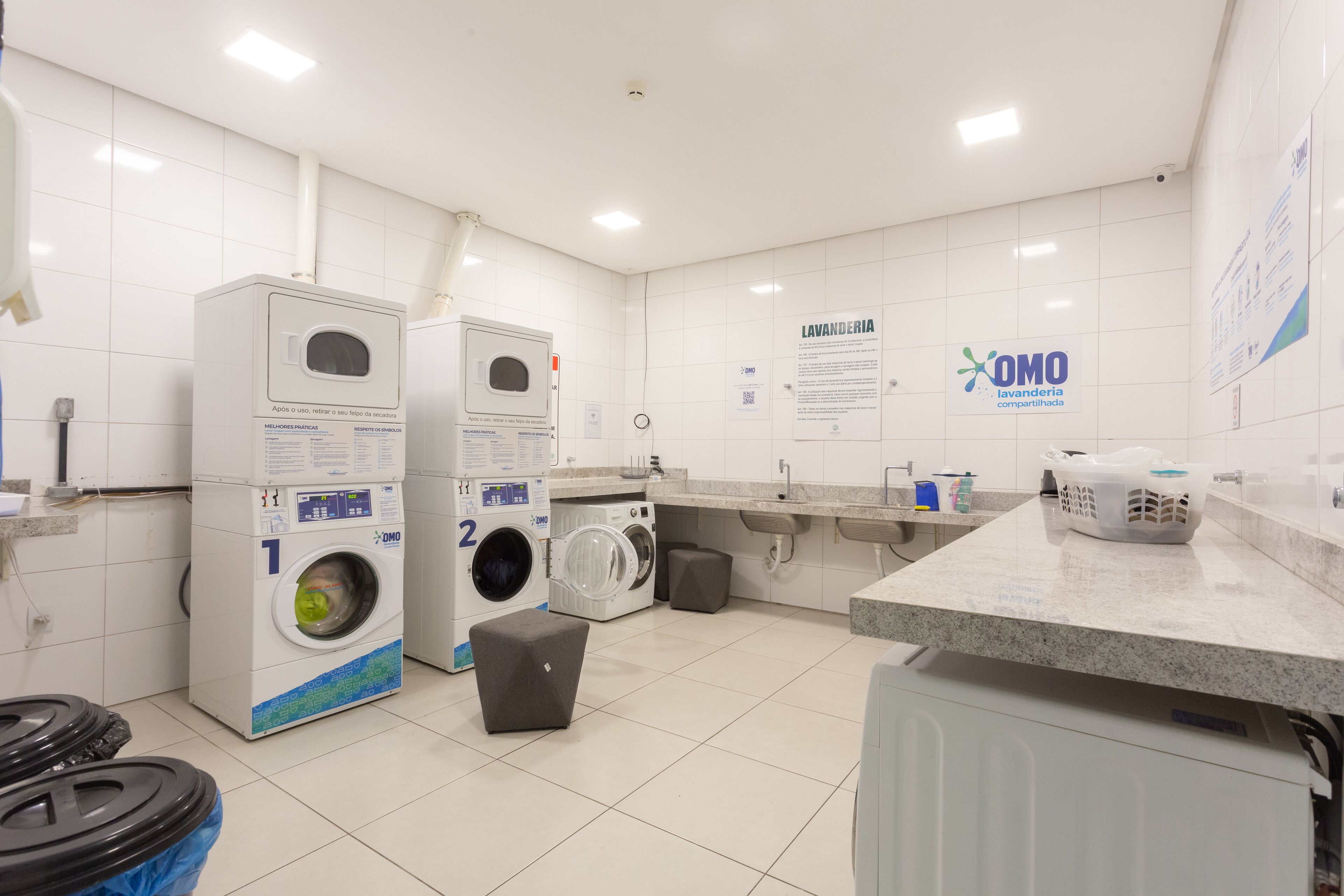 A clean, well-lit laundry room with two washing machines, a drying machine, and a sink.