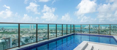 A rooftop infinity pool with a city view, surrounded by glass railings.