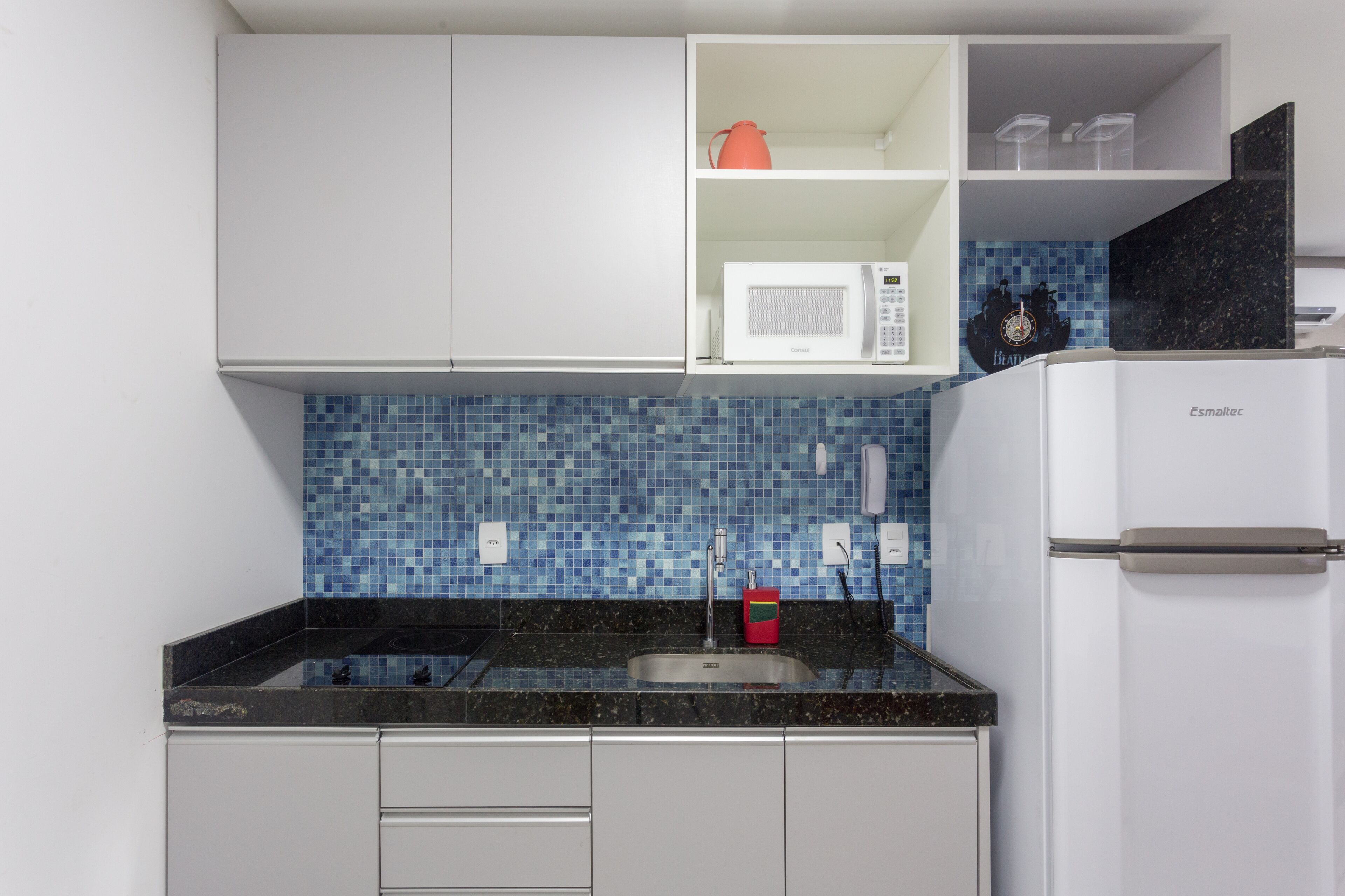 Una cocina con armarios blancos, salpicadero de azulejos azules, microondas blanco y refrigerador blanco.