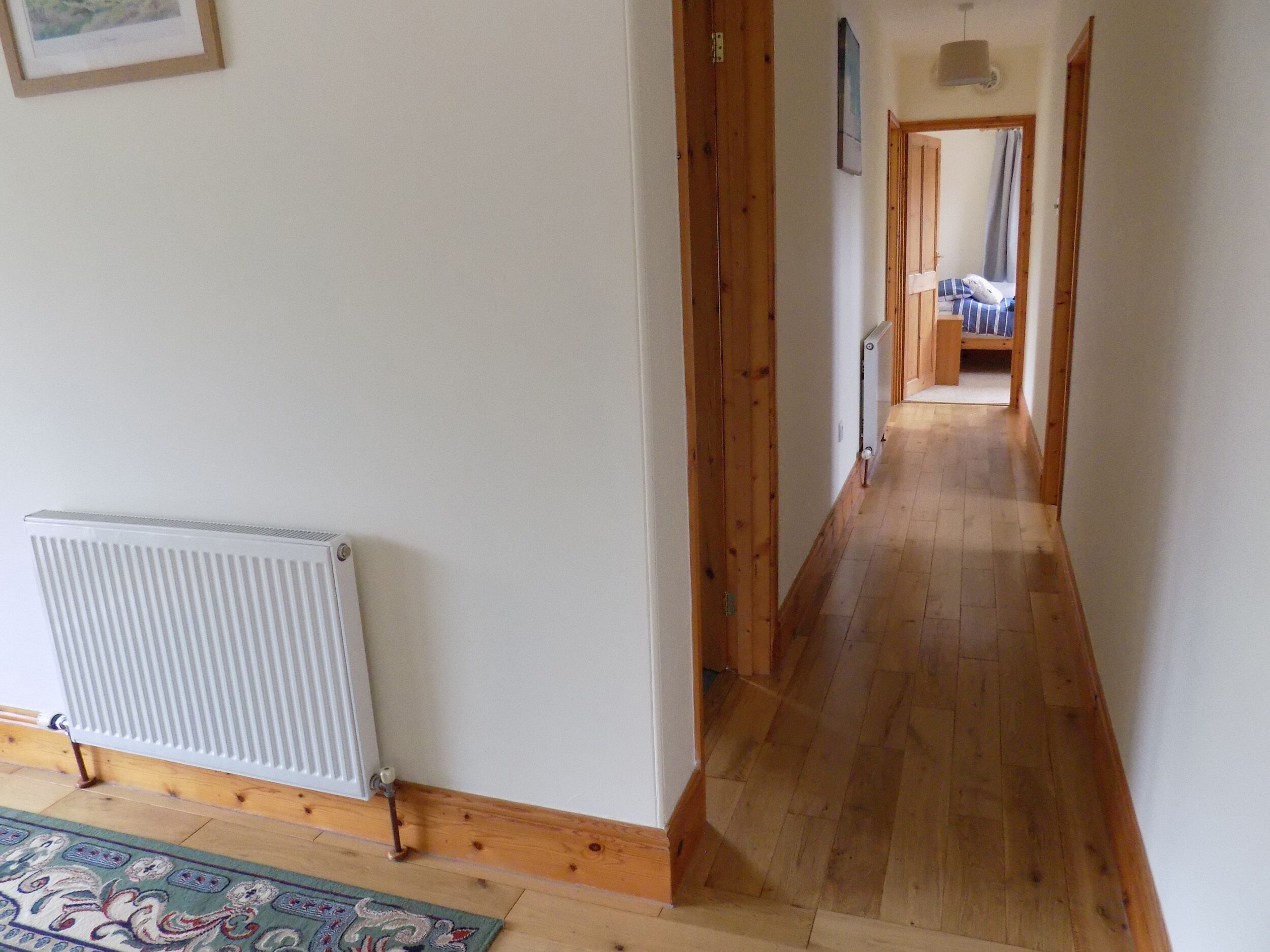 Un couloir étroit, doté d’un plancher en bois et d’un radiateur sur le côté gauche.