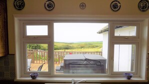 A kitchen with a large window overlooking a deck and a scenic view of rolling hills. - Brookfield (Bude)