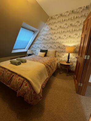 Cozy bedroom with a sloped ceiling and skylight, featuring a forest-themed wallpaper and a comfortable bed.
