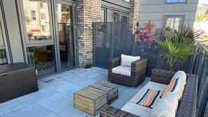 Eine Dachterrasse mit Korbmöbeln, einem Holzschemel und Topfpflanzen.