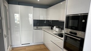 Eine moderne Küche mit weißen Schränken, einer schwarzen Spritzschutzwand und Edelstahlgeräten, darunter ein Backofen und eine Mikrowelle.