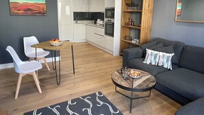 Ein modernes Wohnzimmer mit grauem Sofa, einem Couchtisch und einem Essbereich mit zwei weißen Stühlen.