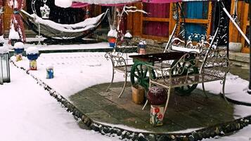 A snow-covered outdoor seating area with a metal table and chairs, surrounded by potted plants and a hammock.