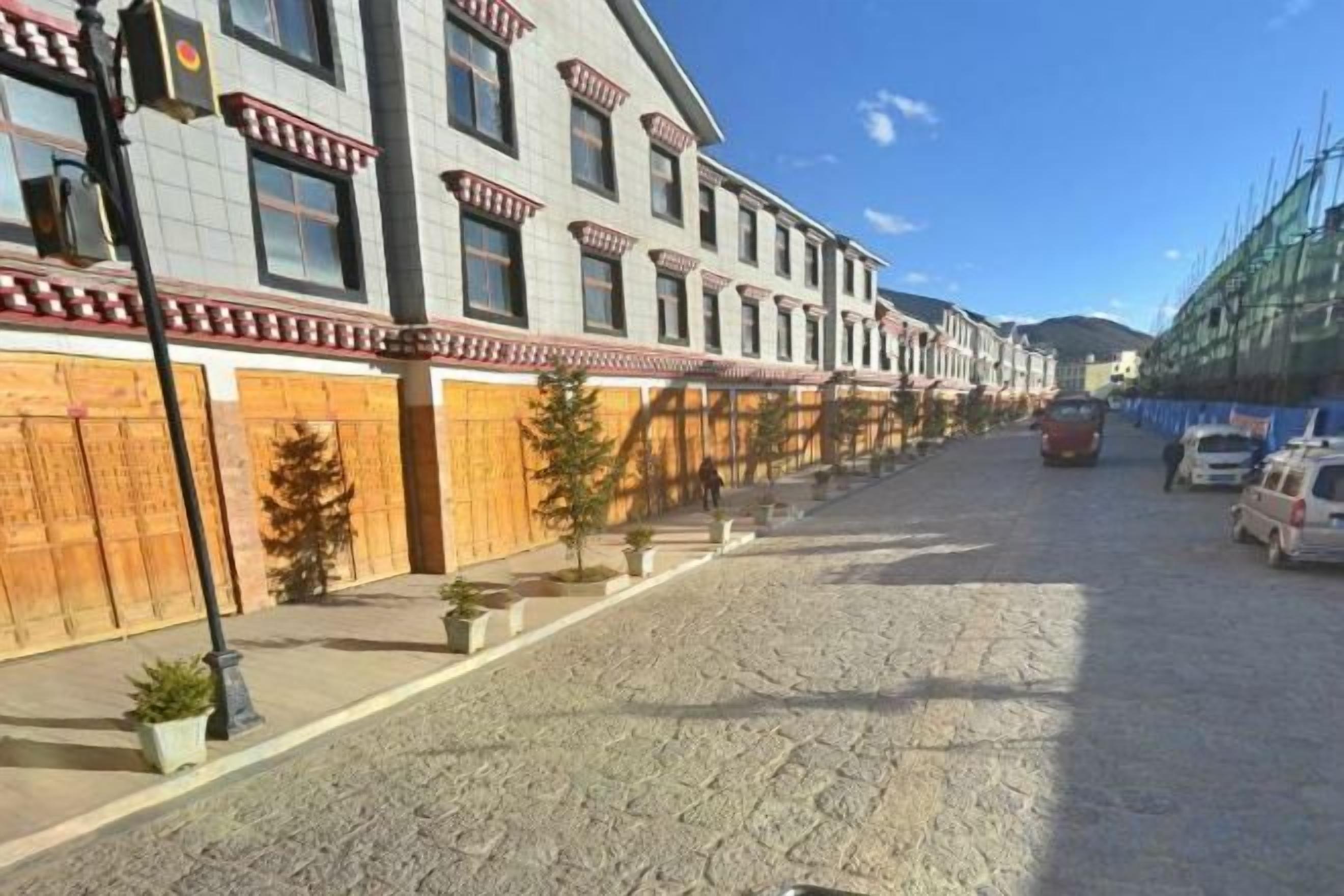 A cobblestone street lined with buildings, a parked car, and a clear sky.