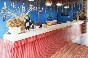 A reception desk with a red tiled counter, decorative plants, and a blue wall with hanging decorations. - Shangri-La Xiangguo Home Inn (Shangri-La)