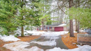 A residential property with a garage, a driveway, and surrounding trees. - Cozy Cottage w/ Sunroom - Walk to Higgins Lake! (Roscommon)