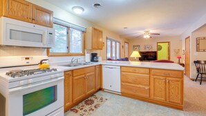A kitchen with wooden cabinets, a microwave, stove, and dishwasher. - Cozy Cottage w/ Sunroom - Walk to Higgins Lake! (Roscommon)