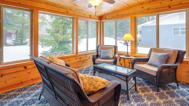 A cozy room with wicker furniture, large windows, and a ceiling fan. - Cozy Cottage w/ Sunroom - Walk to Higgins Lake! (Roscommon)