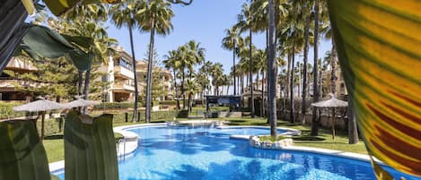 A swimming pool surrounded by palm trees and a building with a poolside area.