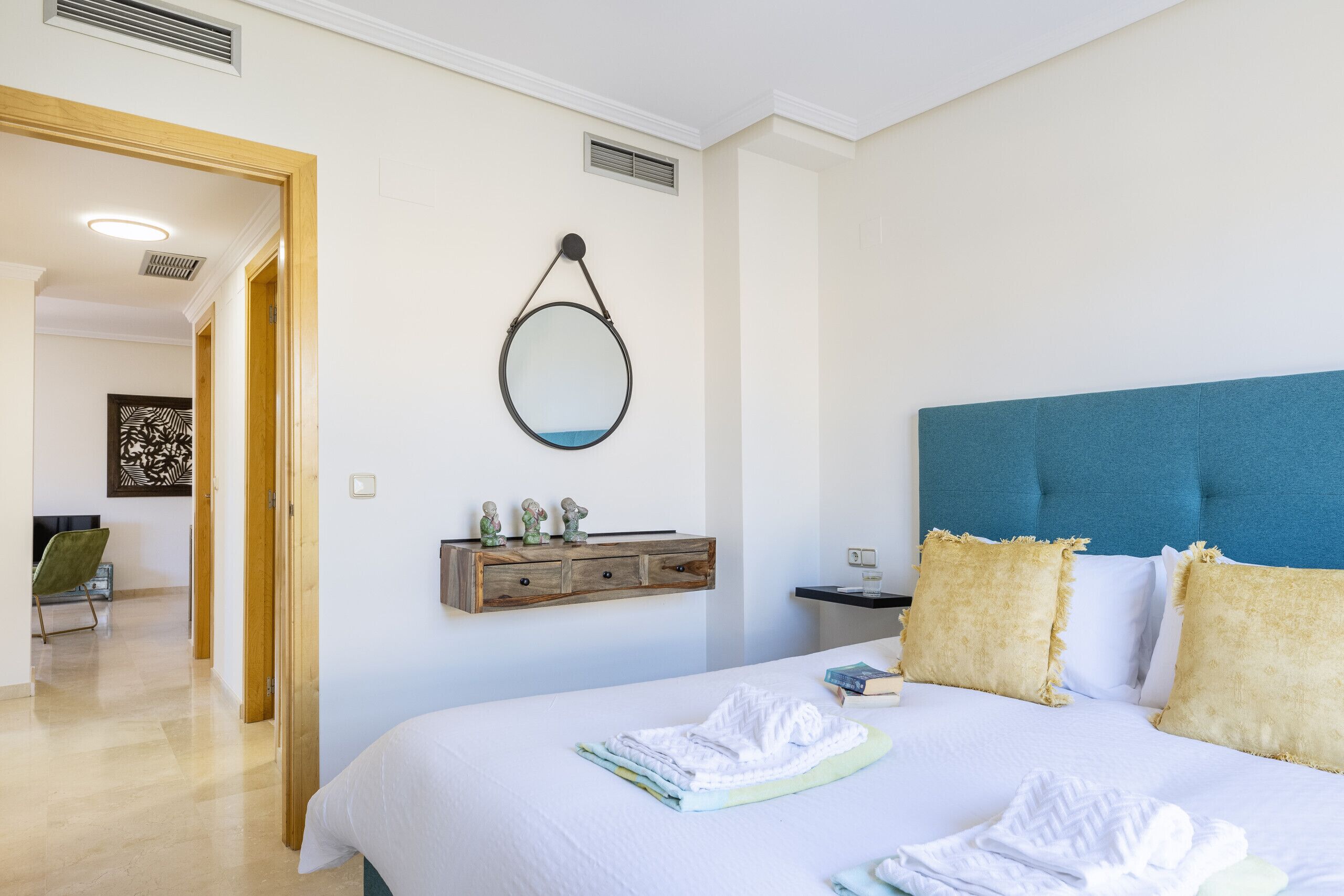 Un dormitorio ordenado con cama, mesita de noche y un espejo montado en la pared.