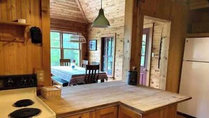 A wooden cabin kitchen with a central island, wooden cabinets, a stove, and a refrigerator. - Hilltop Cottage (Argyle)