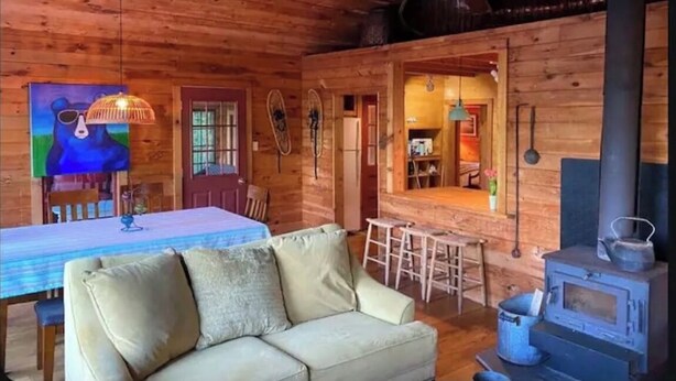 A cozy log cabin interior with a sofa, dining table, and a wood-burning stove. - Hilltop Cottage (Argyle)