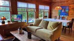 A cozy cabin interior with a sofa, a coffee table, a TV, and a dining area with a table and chairs. - Hilltop Cottage (Argyle)