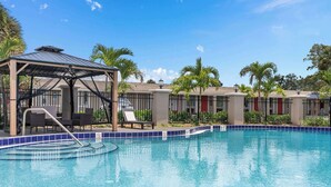A clear blue swimming pool with a covered seating area and lounge chairs. - Travelodge by Wyndham Kissimmee/Orlando (Kissimmee)