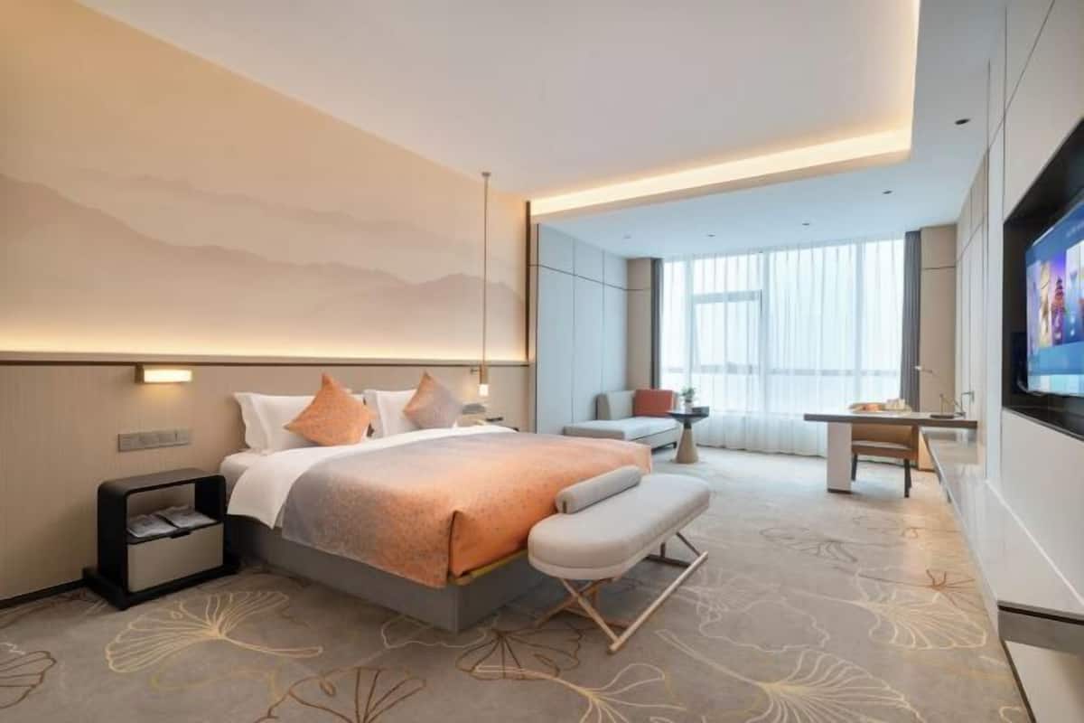 A modern hotel room with a large bed, a desk, a chair, and a TV.