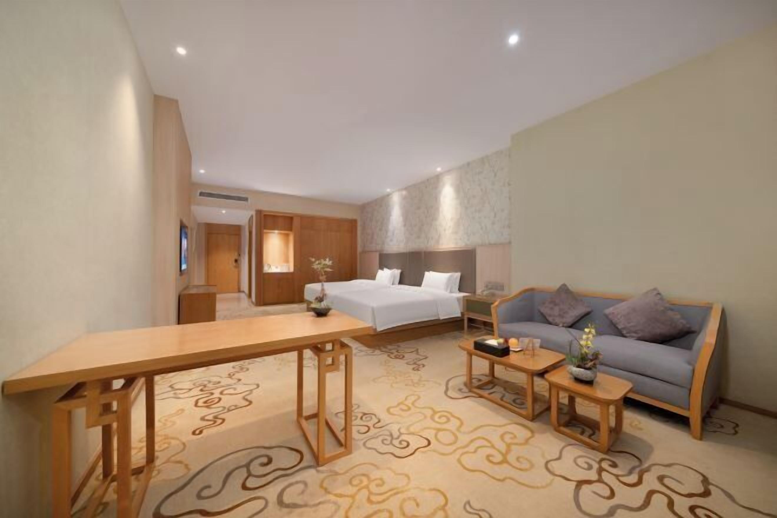 A hotel room with a bed, a sofa, a wooden table, and a small side table.