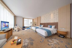 Habitación de hotel con dos camas, televisión, escritorio, silla y una mesita con frutas.