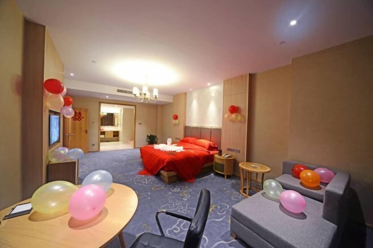 Una habitación de hotel con una cama, un escritorio adornado con globos, una silla, una mesita y un sofá.