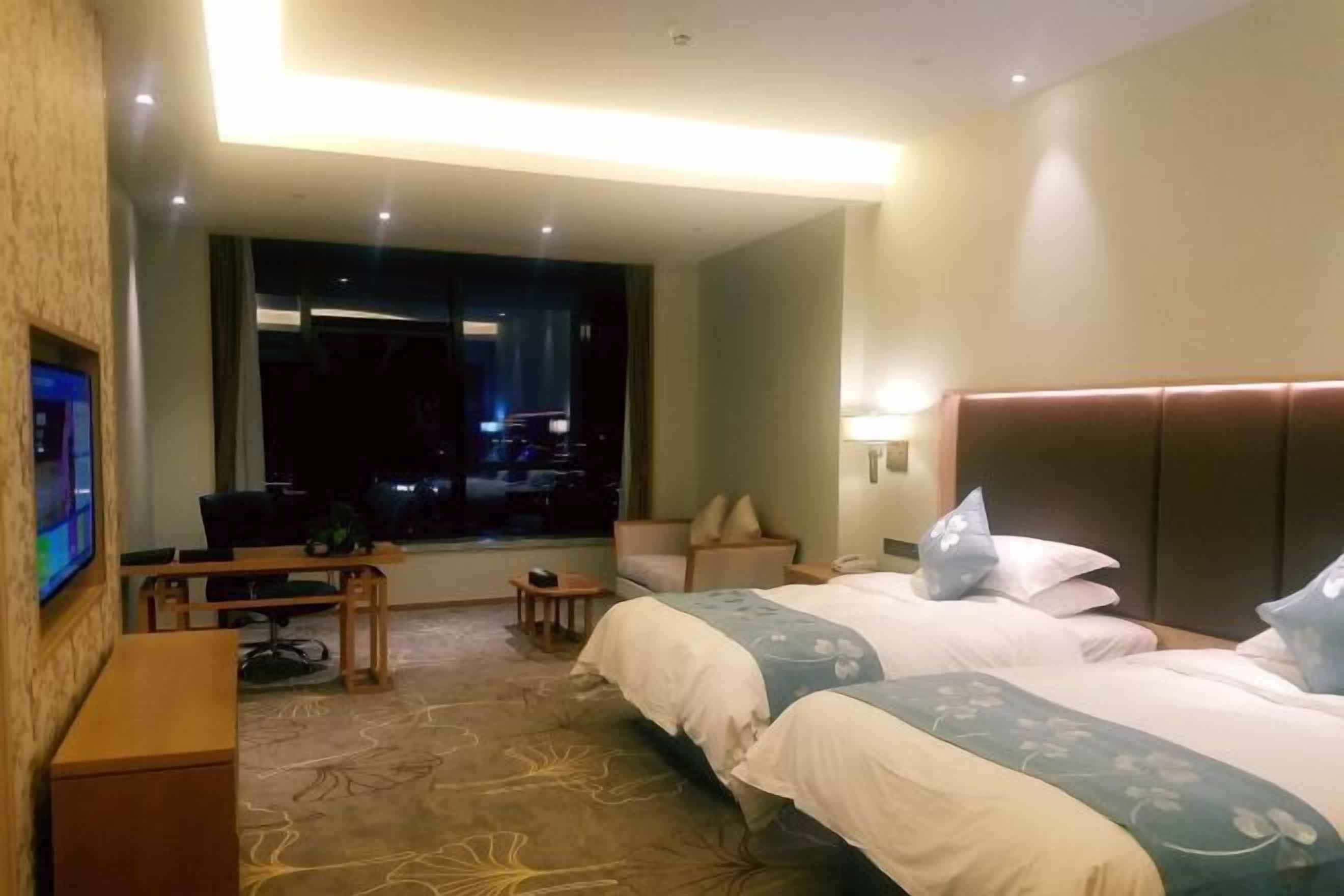A hotel room with two beds, a desk, a chair, a TV, and a window with a city view.