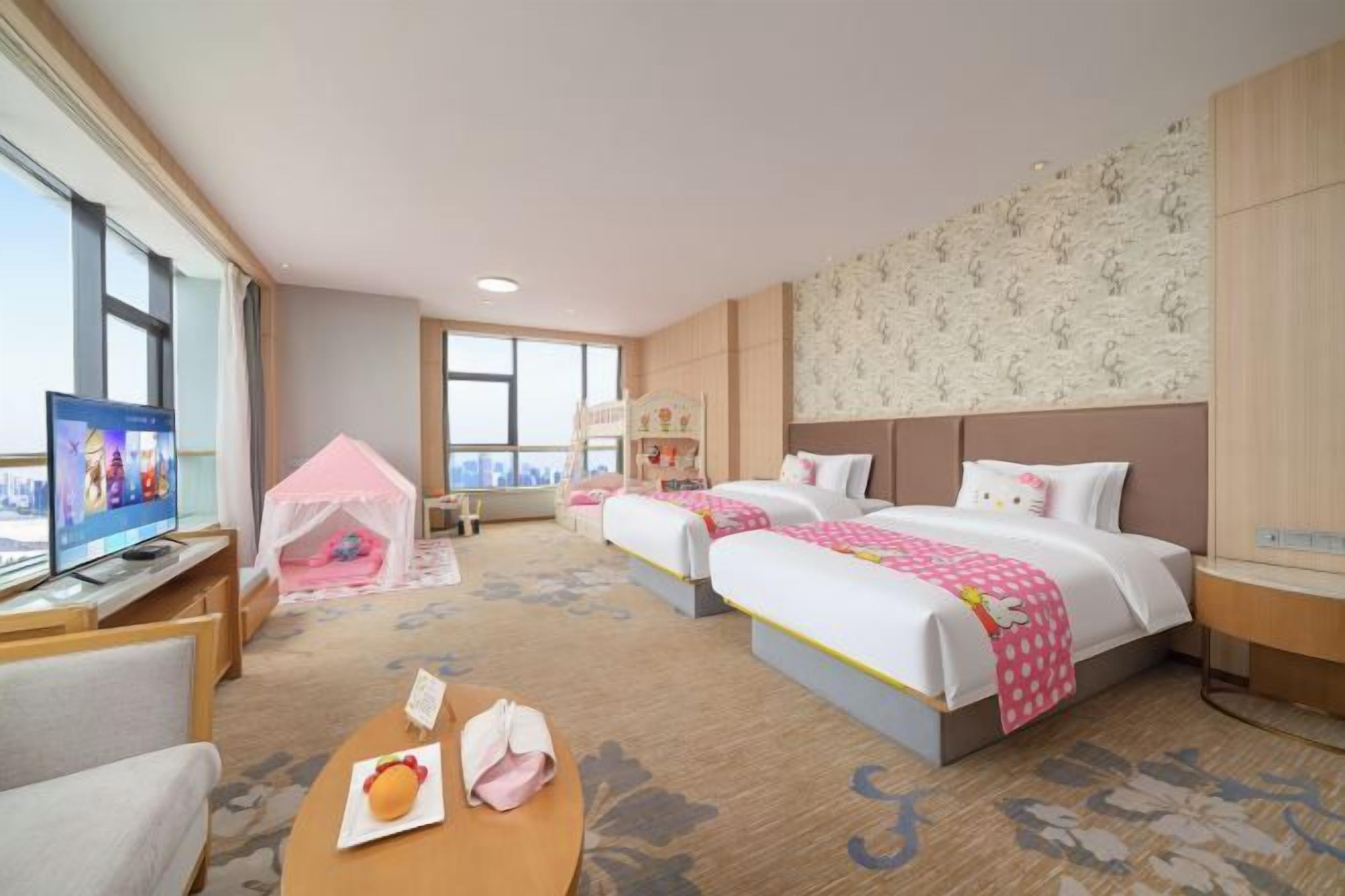 Quarto de hotel com duas camas, televisão, escrivaninha e um laptop, e vista para a cidade.