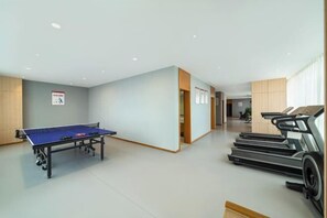 Une pièce équipée d’une table de ping-pong, de tapis de course et d’une armoire en bois.