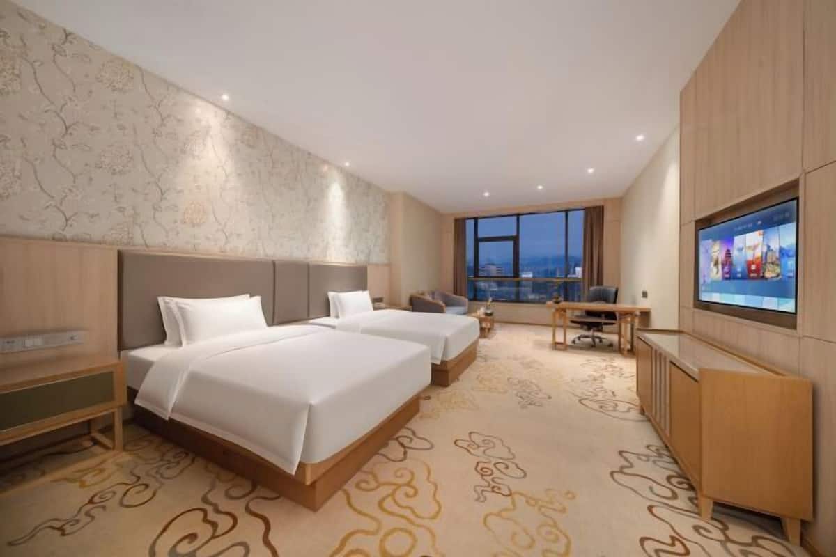A hotel room with two beds, a TV, a desk, and a large window with a view.