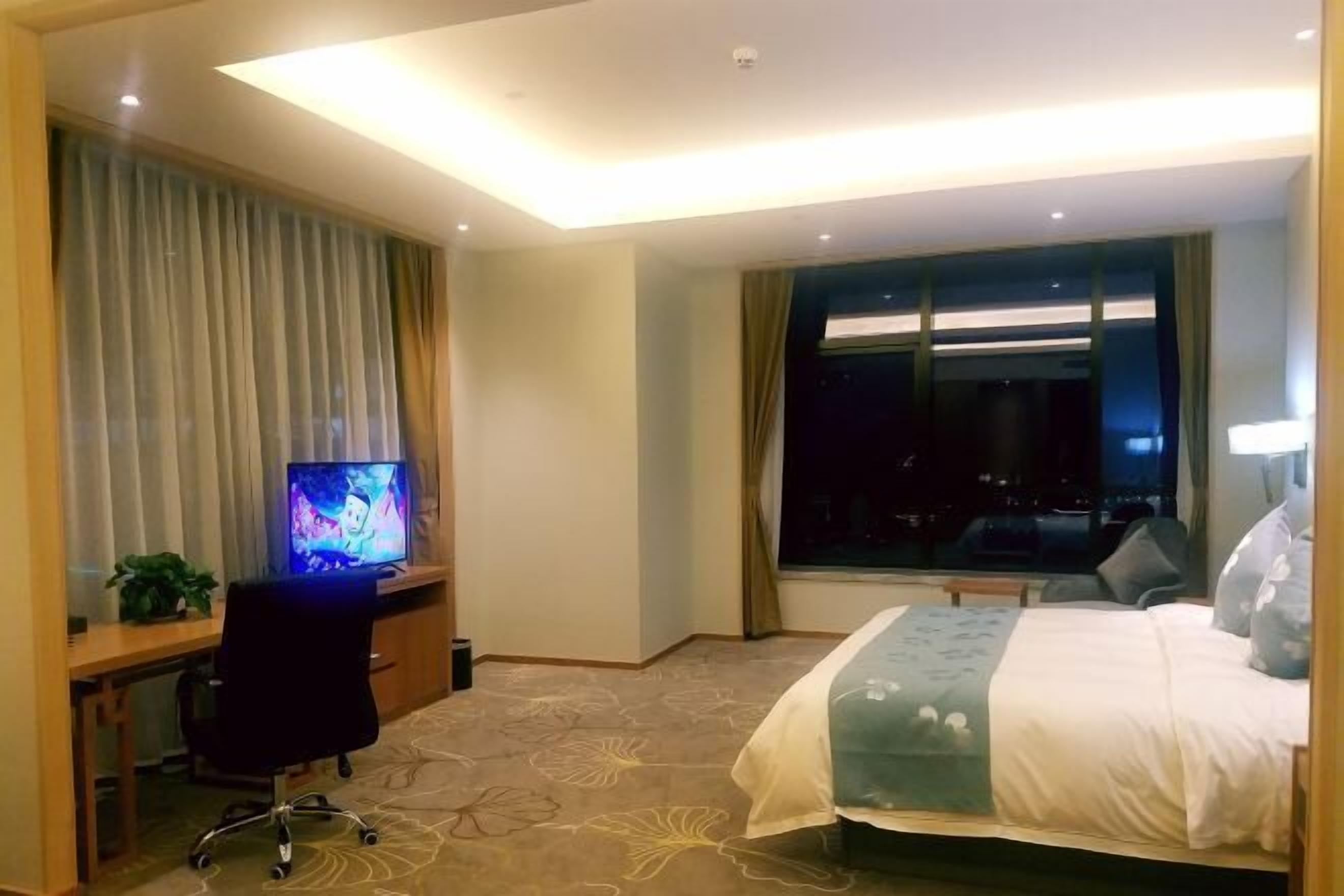 A hotel room with a bed, a desk with a computer, a window, and a view of the city at night.