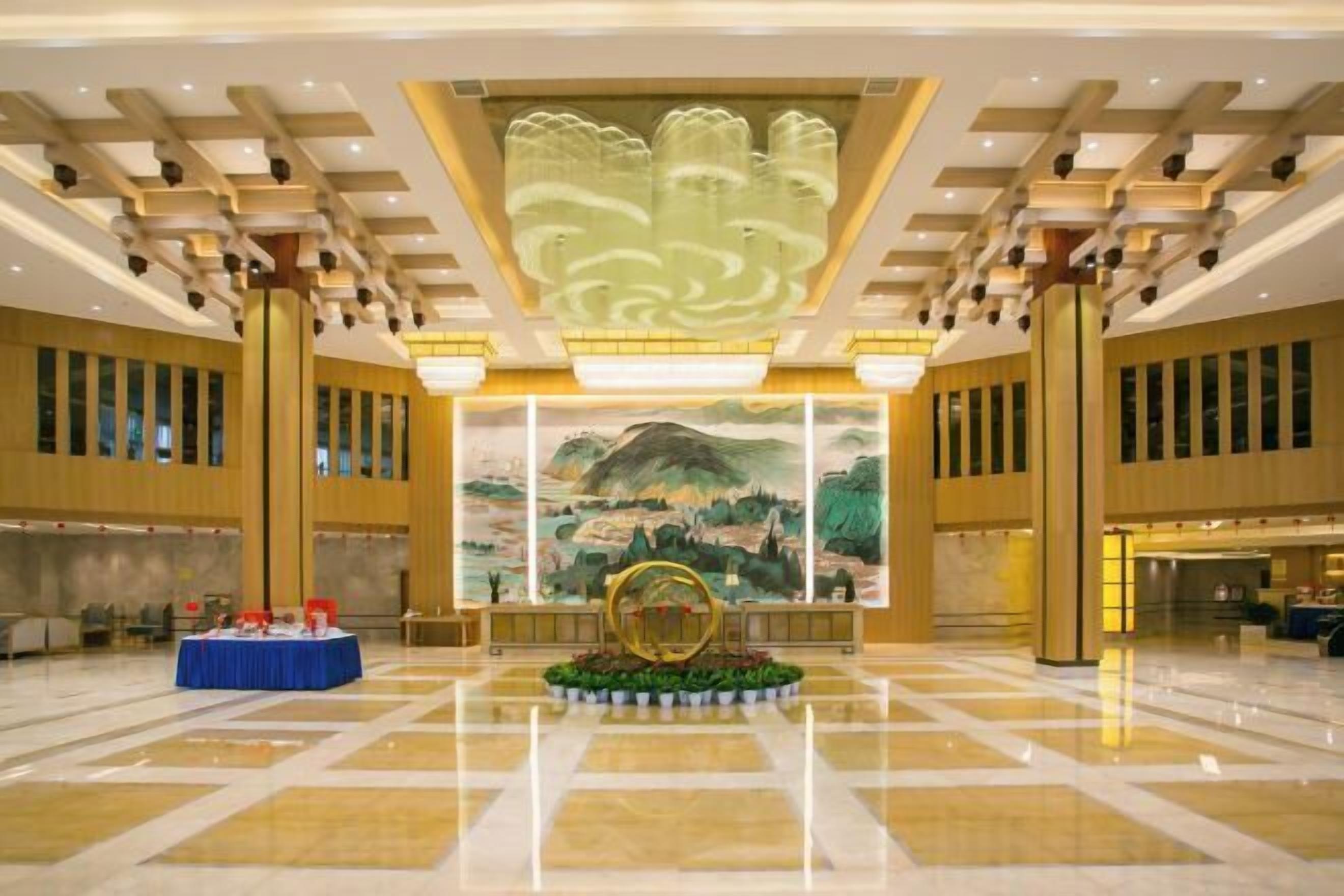 A spacious lobby with a large mural, a central decorative fountain, and a reception desk.