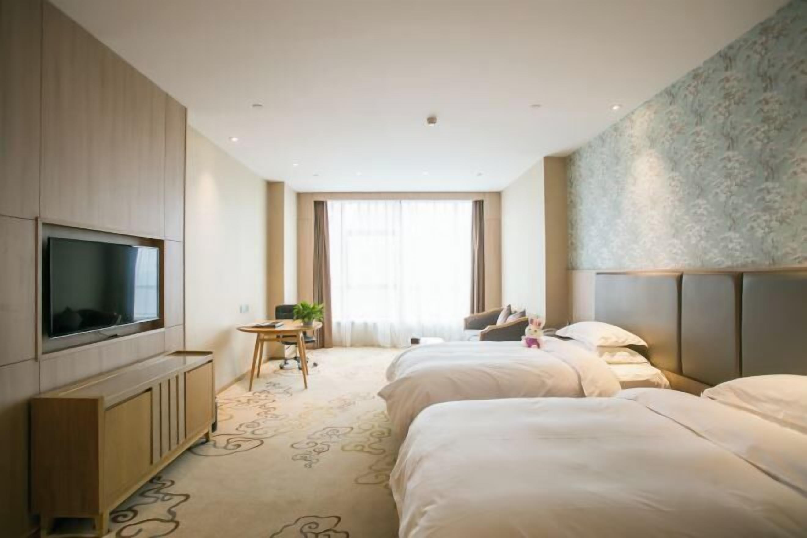 A hotel room with a TV, two beds, a desk, and a large window.