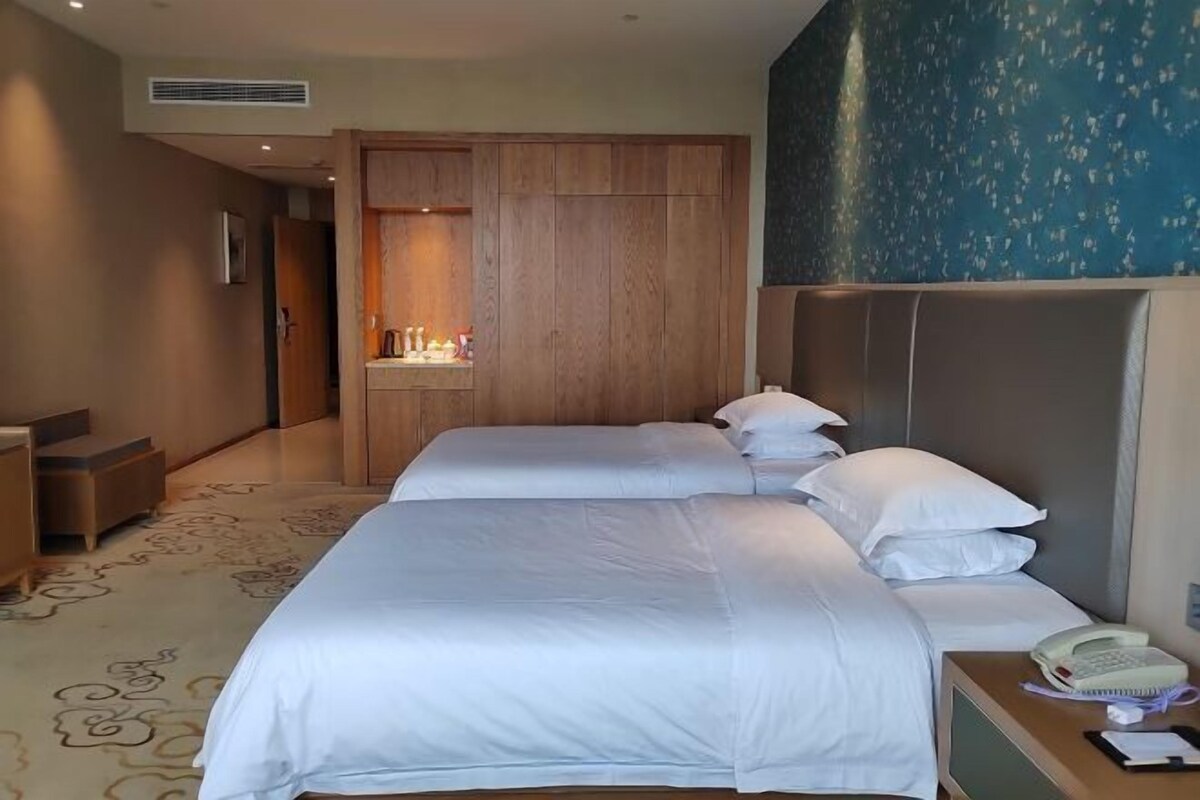 Habitación de hotel con dos camas, un armario de madera, una mesita de noche con teléfono y una pared con un diseño azul.