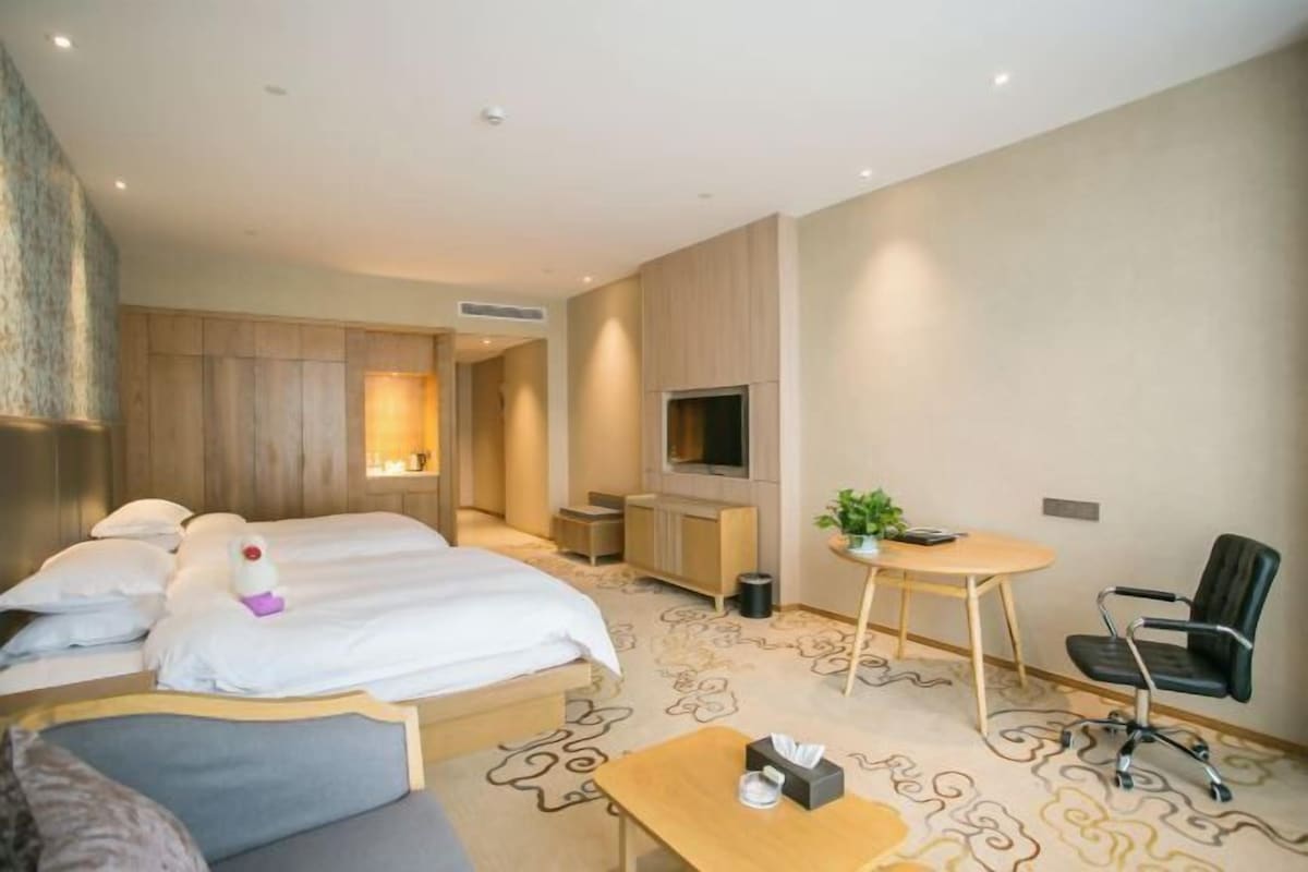 Habitación de hotel con dos camas, un sofá, una mesita, un televisor y una planta.