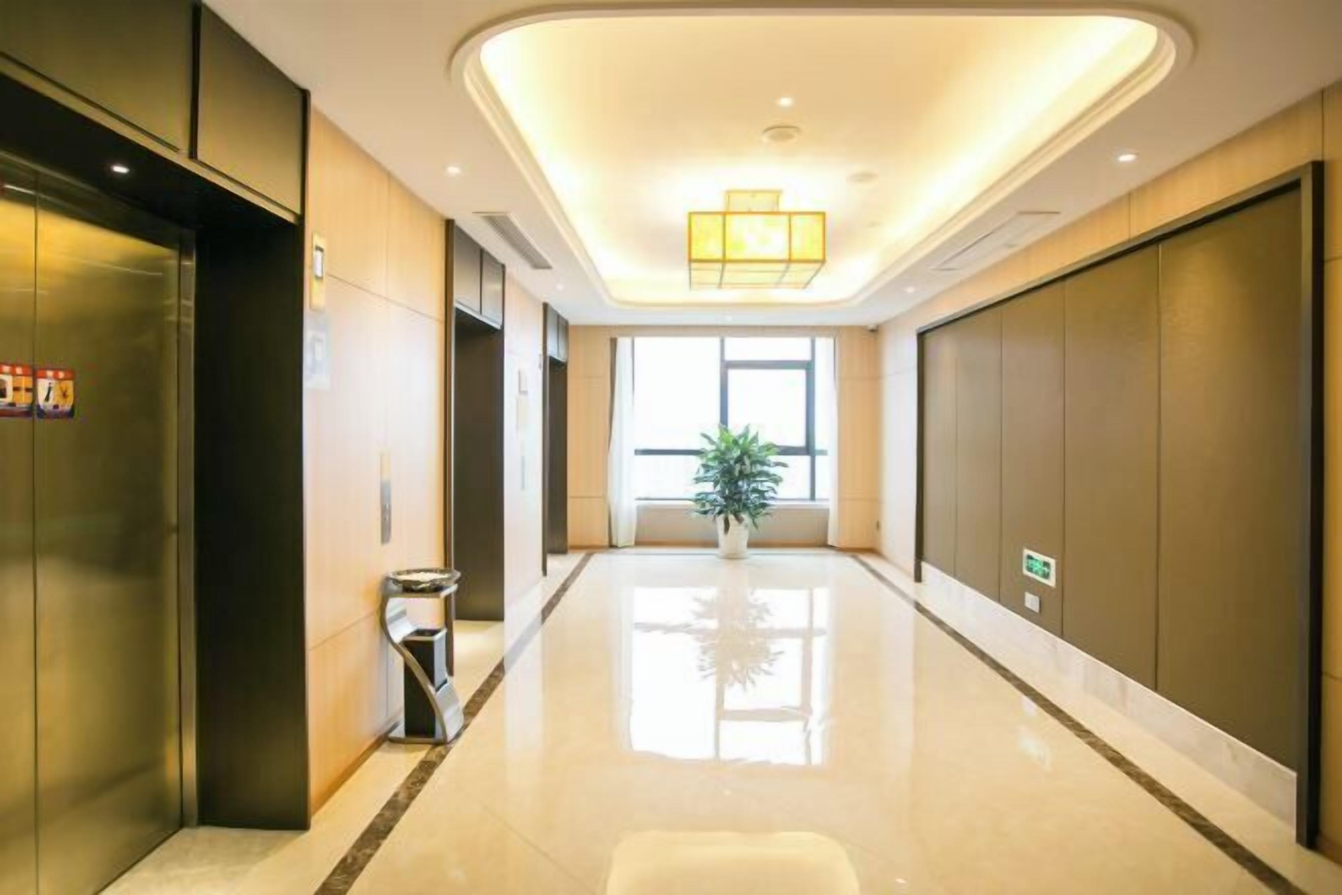 A modern hotel lobby with a shiny floor, a central potted plant, and a large window.