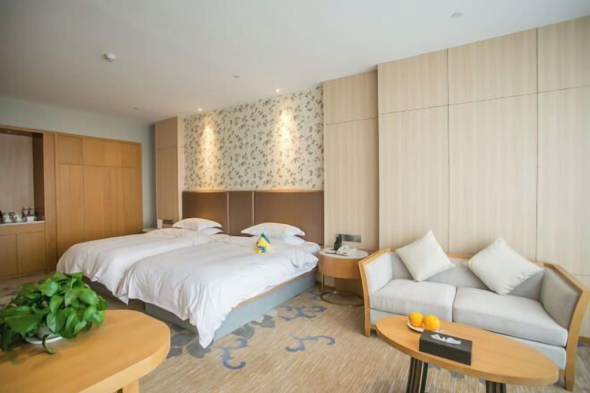 Una habitación de hotel con una cama, un sofá, una mesita y una planta.
