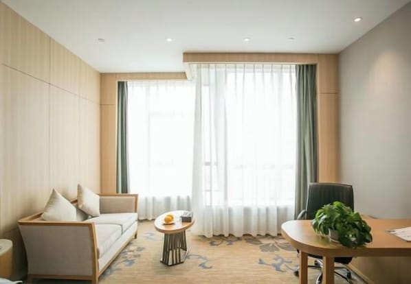 Una habitación de hotel moderna con un sofá, una mesita redonda con frutero, una silla y una planta en maceta.