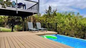 Um deck de madeira com piscina, cadeiras de descanso e área coberta com assentos.
