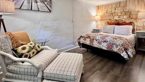 Ein Schlafzimmer mit einem Bett, einem Sessel, einem kleinen Tisch und einem an der Wand befestigten Fernseher.