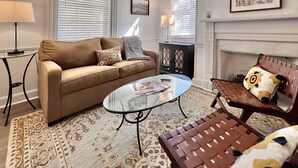 Ein Wohnzimmer mit einem beigen Sofa, einem Glastisch, einem gemusterten Teppich, einem Beistelltisch und einer Bank mit Kissen.