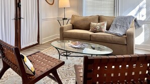 Ein Wohnzimmer mit einem beigen Sofa, einem Glastisch, einer Holzbank und einem gemusterten Teppich.